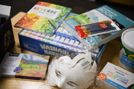 paper masks a large box of markers colored pencils coloring books and modeling clay sit on a tabletop