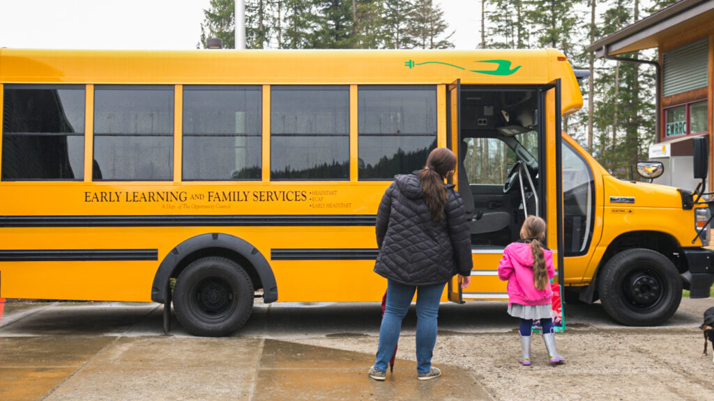 A mother and child look at a yellow school bus with "Early Learning and Family Services" written on it.