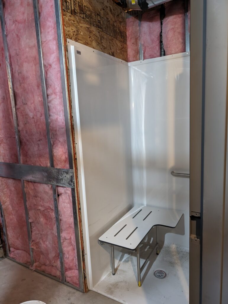 Shower insert set within unfinished walls full of pink insulation.