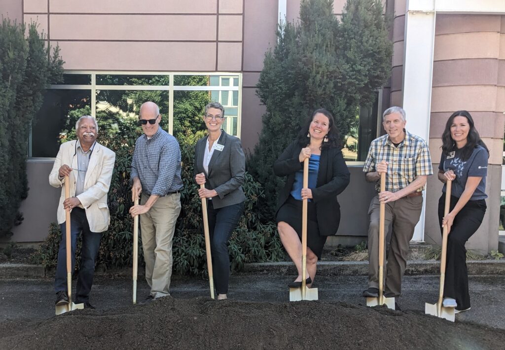 A group of elected officials and Way Station partnering organization representatives stand in a line with golden shovels in front of a building.
