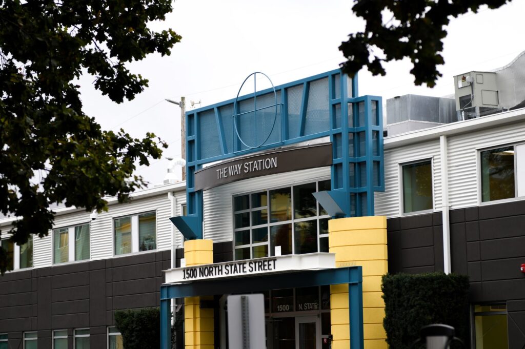 A grey building with blue and yellow accents framed by oak trees.