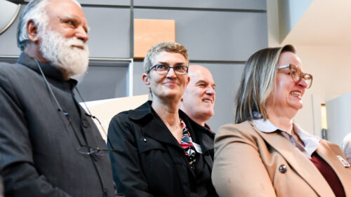 A group of men and women in suits smile proudly inside a room