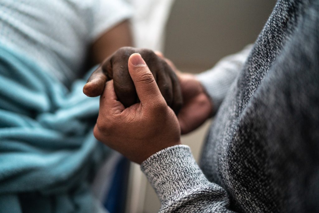 A person holds the hand of someone in a hospital bed.